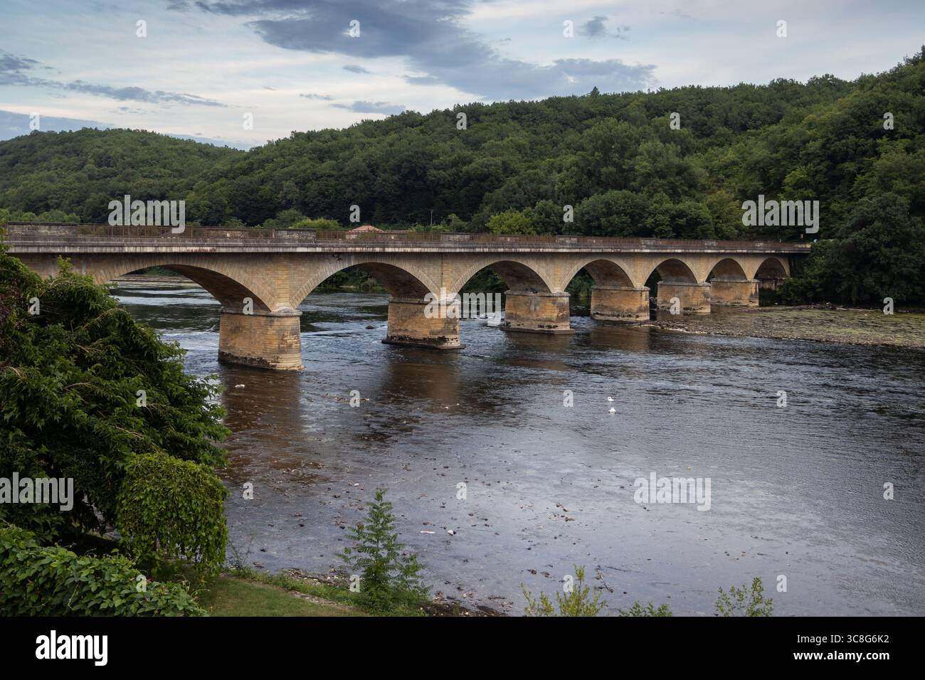 The 19th century Pont de Lalinde, the arched road bridge which spans the Dordogne River at Lalinde, in Nouvelle-Aquitaine, France. Copy space below. - Stock Image