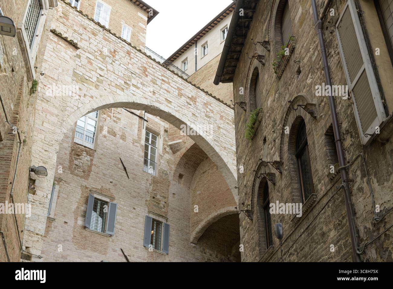 Archway connecting two historical buildings in Perugia, Italy, featuring ancient stone walls and windows with shutters Stock Photo