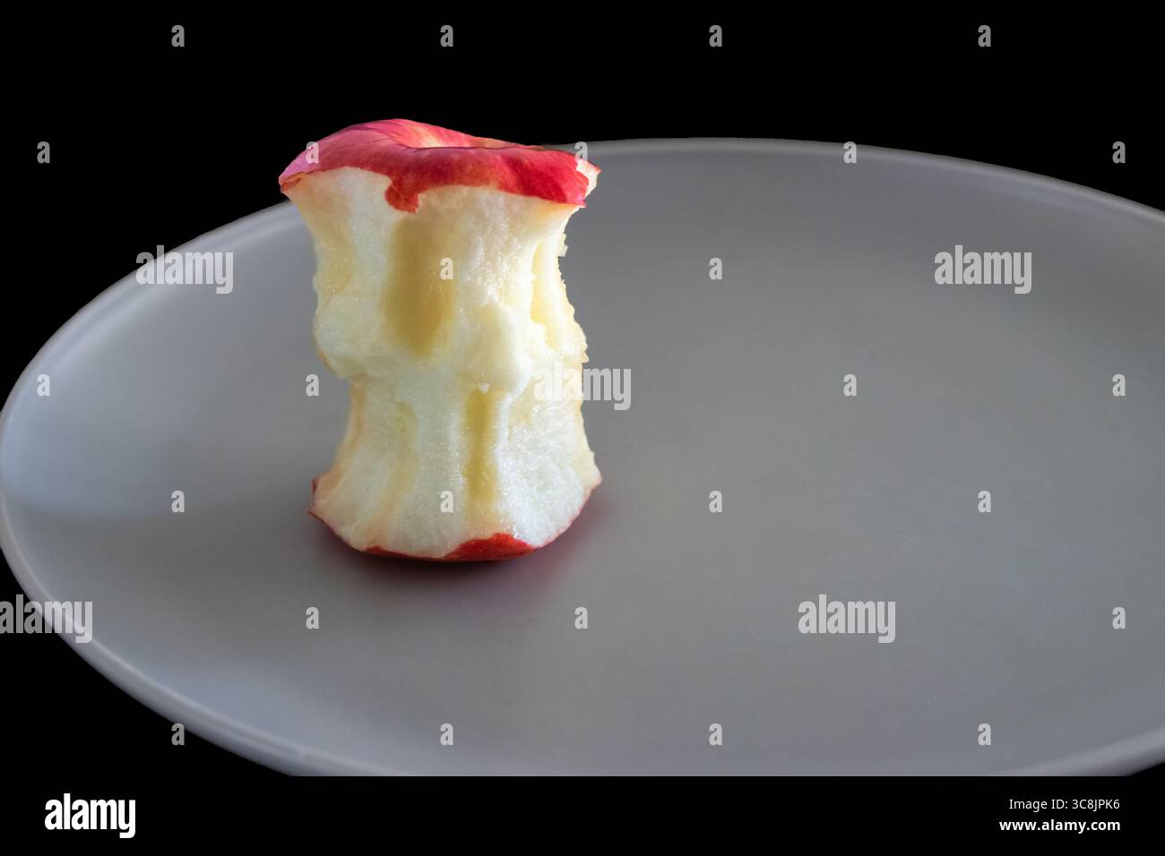 A bitten red apple on a grey plate with a black background Stock Photo