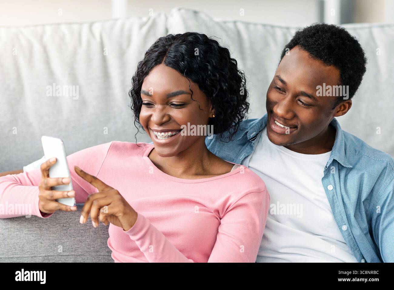Black lovers with cleaning tools sitting on floor, using smartphone Stock Photo