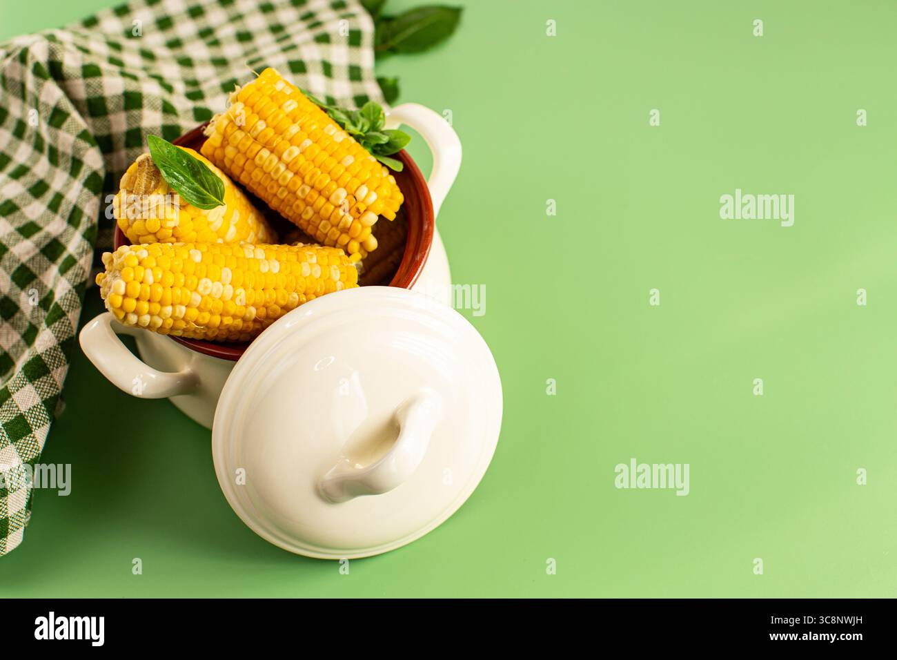Hot corn cobs with greens on a green background. Stock Photo