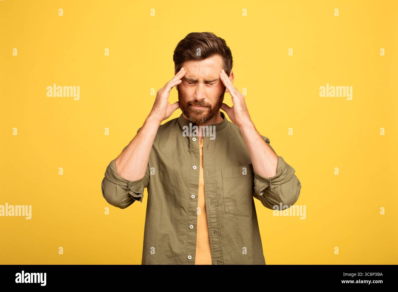 Man experiencing stress while standing against a yellow background Stock Photo
