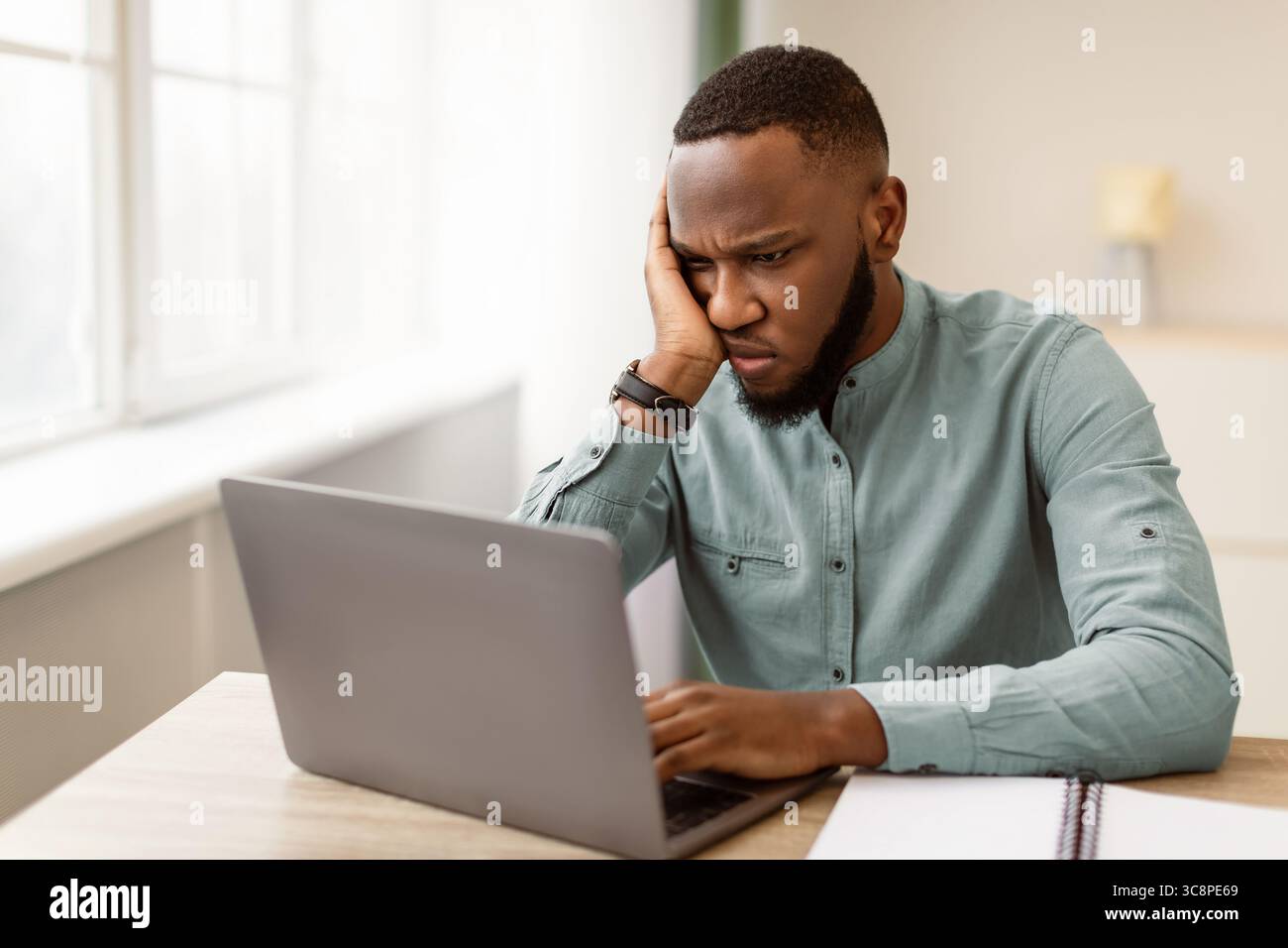 Unhappy Black Businessman Looking At Laptop Sitting At Workplace Indoor Stock Photo