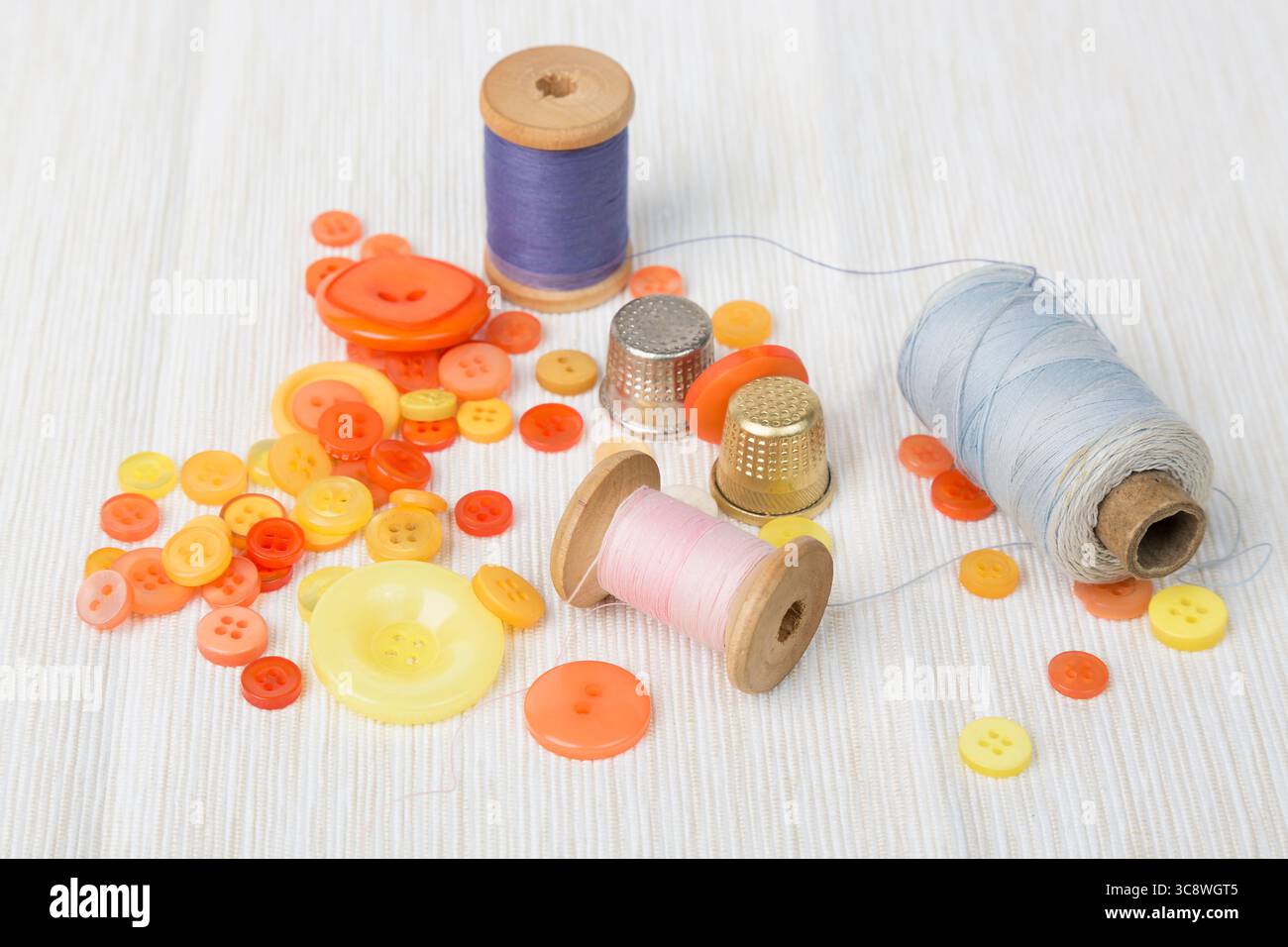 Different thread spools with colorful buttons and thimbles on light surface. Stock Photo