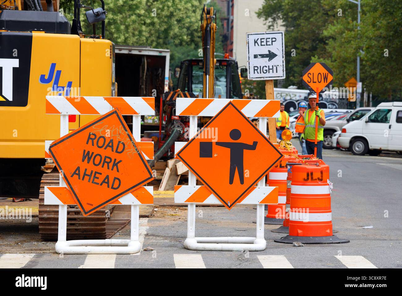 A Road Work Ahead orange warning sign, and a traffic controller, or construction flagger, holding a slow sign at a construction work zone in New York Stock Photo