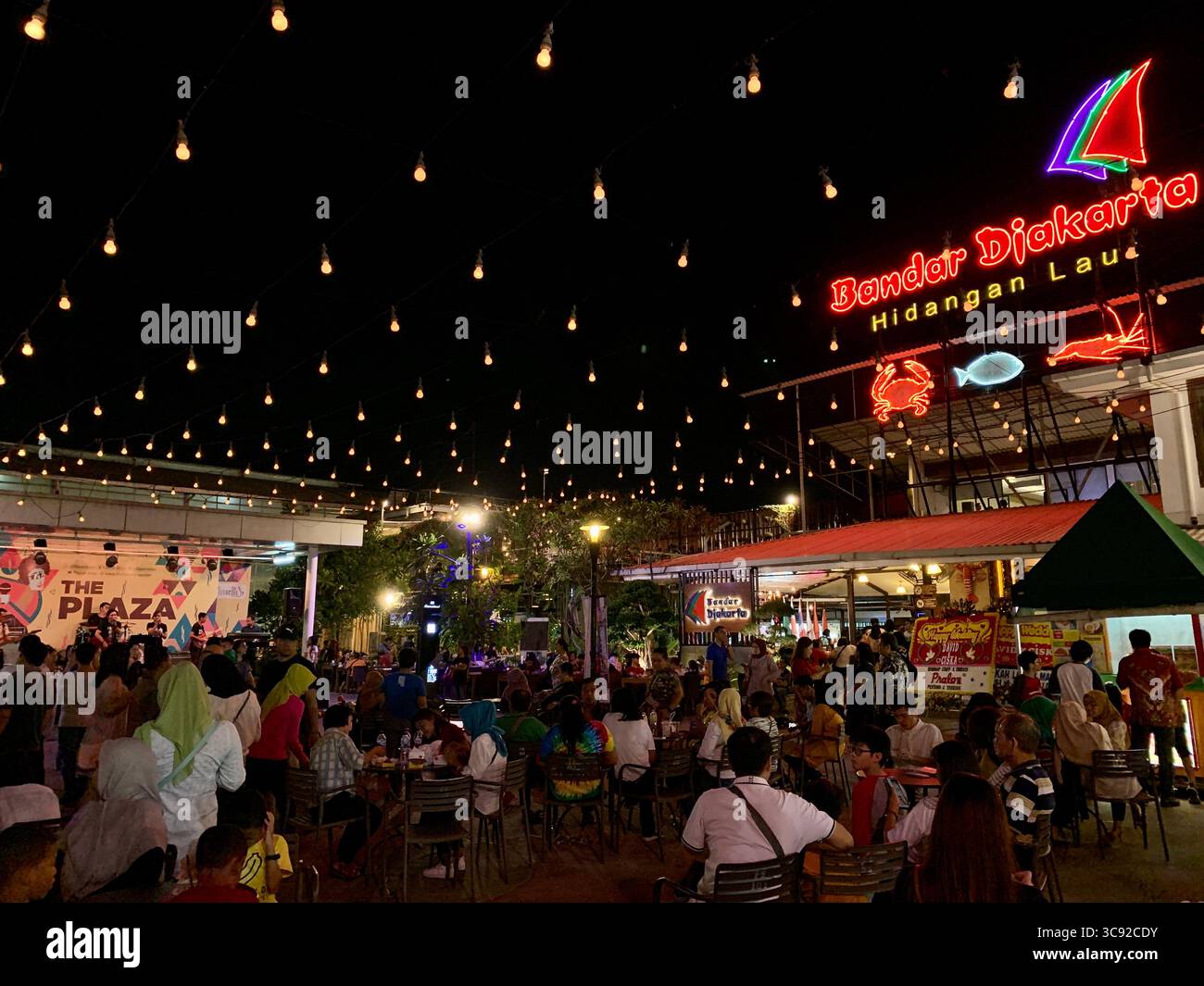 Crowded night market dinner at Bandar Djakarta's outdoor food court with string lights and live music. - Smartphone Captured Stock Image