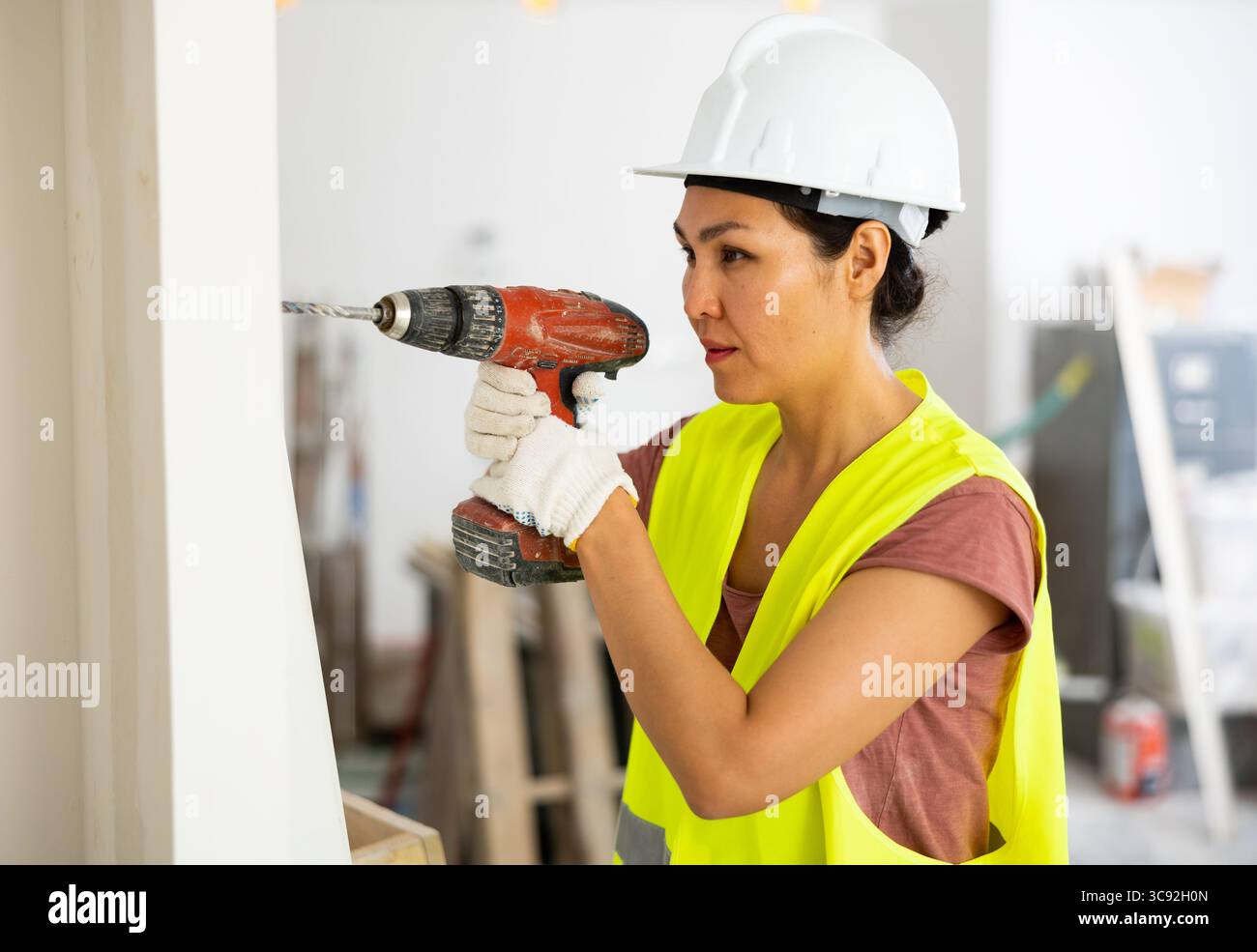 Woman builder using drill to bore hole in wall Stock Photo