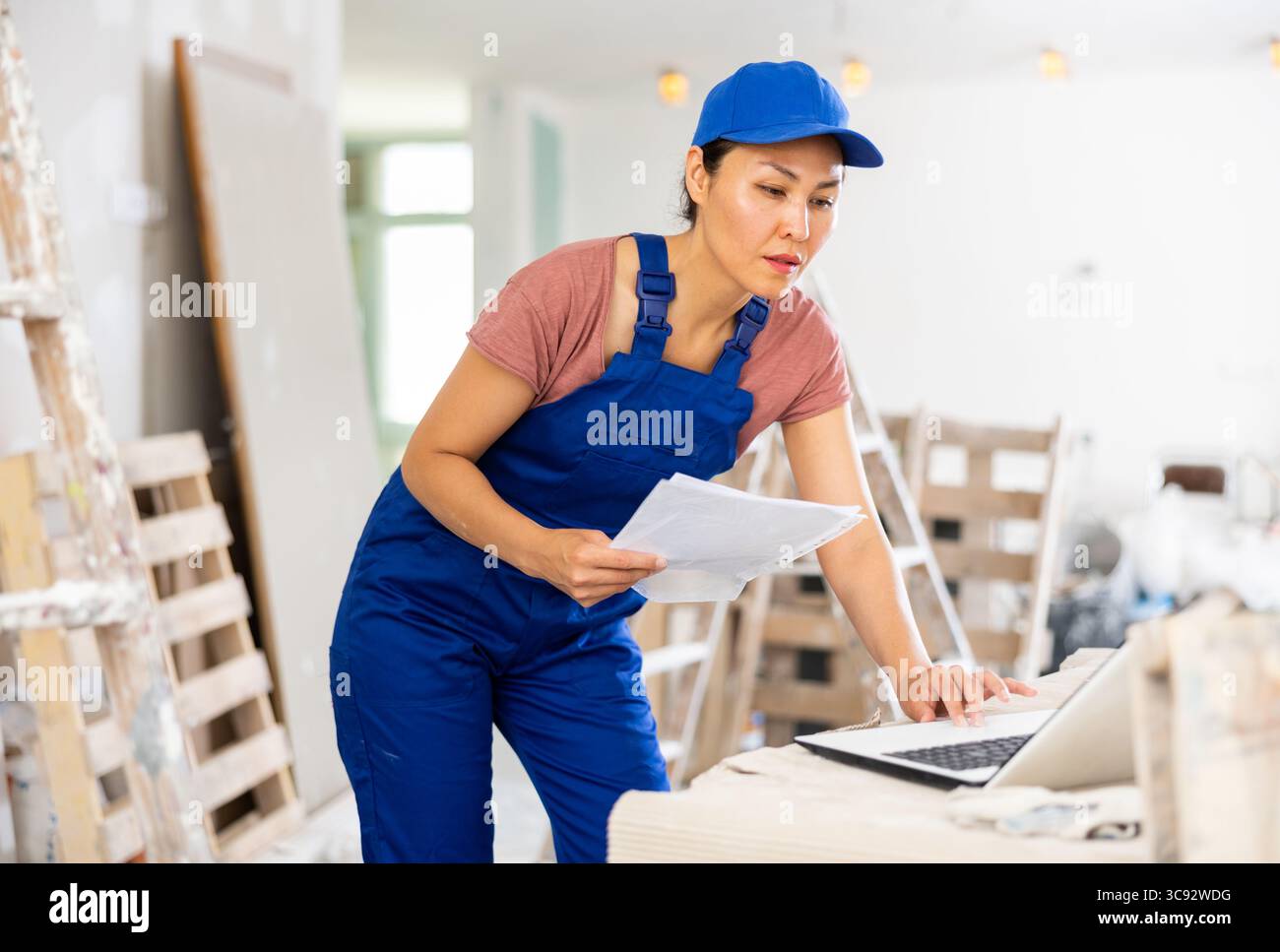 Woman builder checking documentation, using laptop Stock Photo