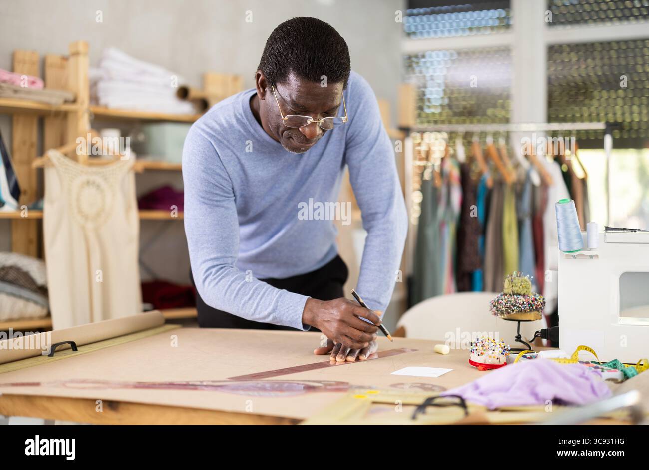 Male tailor draws sketch of future clothing on paper using patterns in ...