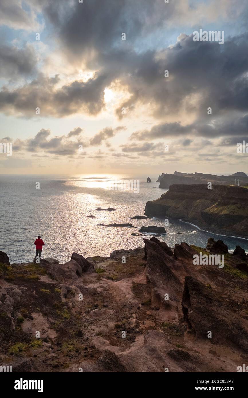 Aerial view of a tourist admiring sunrise over Sao Lourenco peninsula from Miradouro do Calhau da Furna do Bode. Madeira, Portugal, Europe. Stock Photo