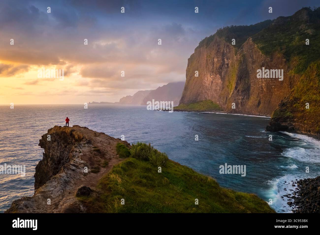 Aerial view of a tourist admiring sunrise from the cliffs of Miradouro do Guindaste. Madeira, Portugal, Europe. Stock Photo