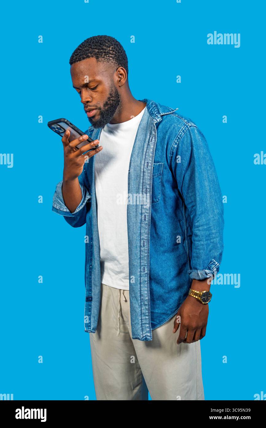 Young man using smartphone, recording voice message on blue background Stock Photo