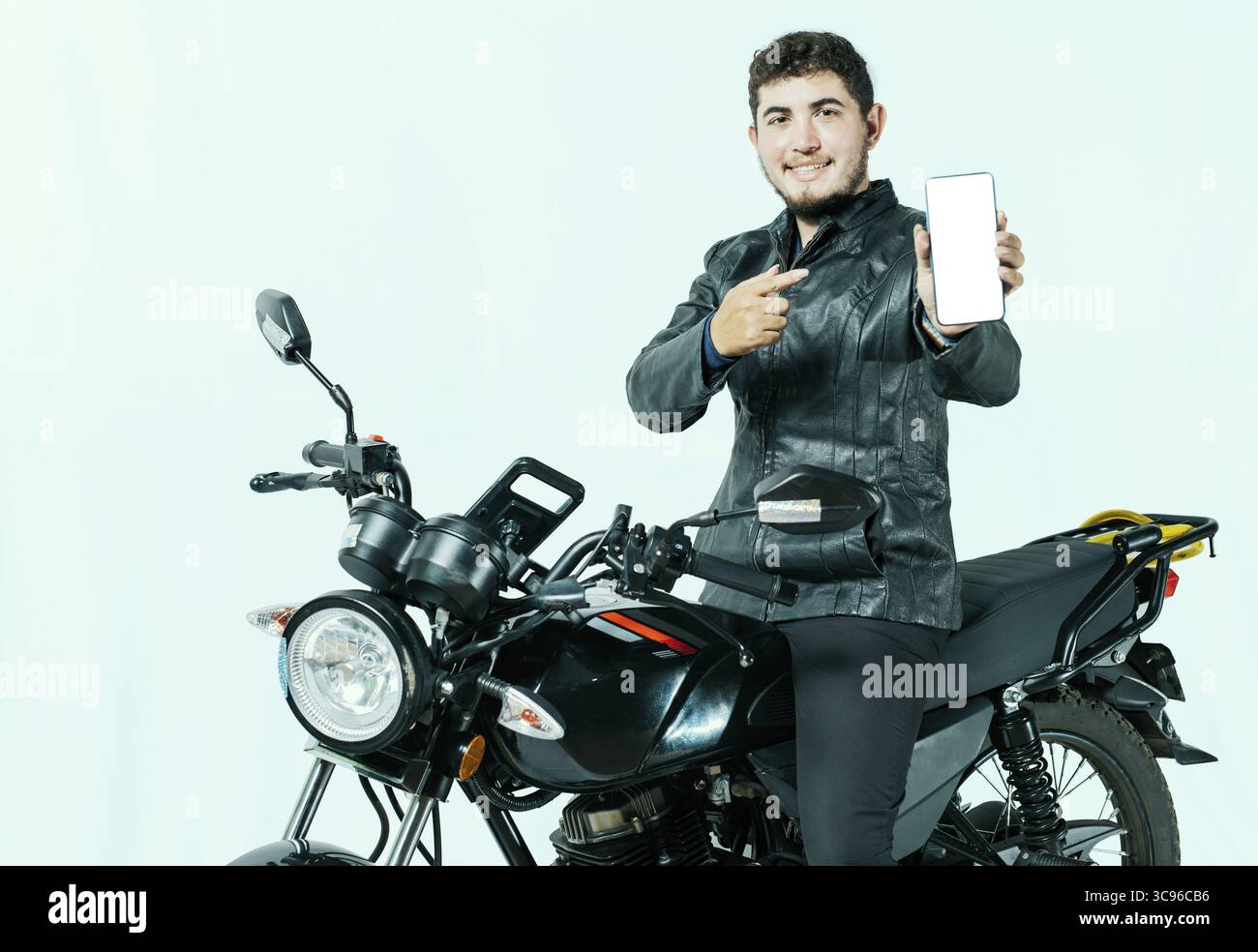 Young motorcyclist sitting on his motorcycle showing cell phone screen isolated. Male biker on his motorcycle showing phone screen Stock Photo