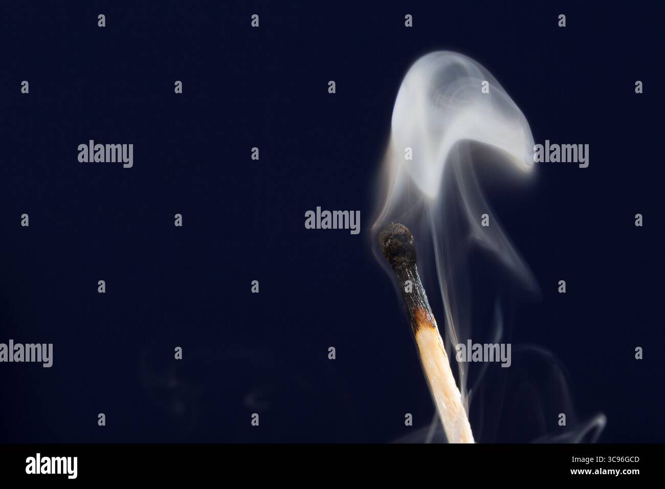 Extinguished match close up with smoke on dark blue background Stock Photo