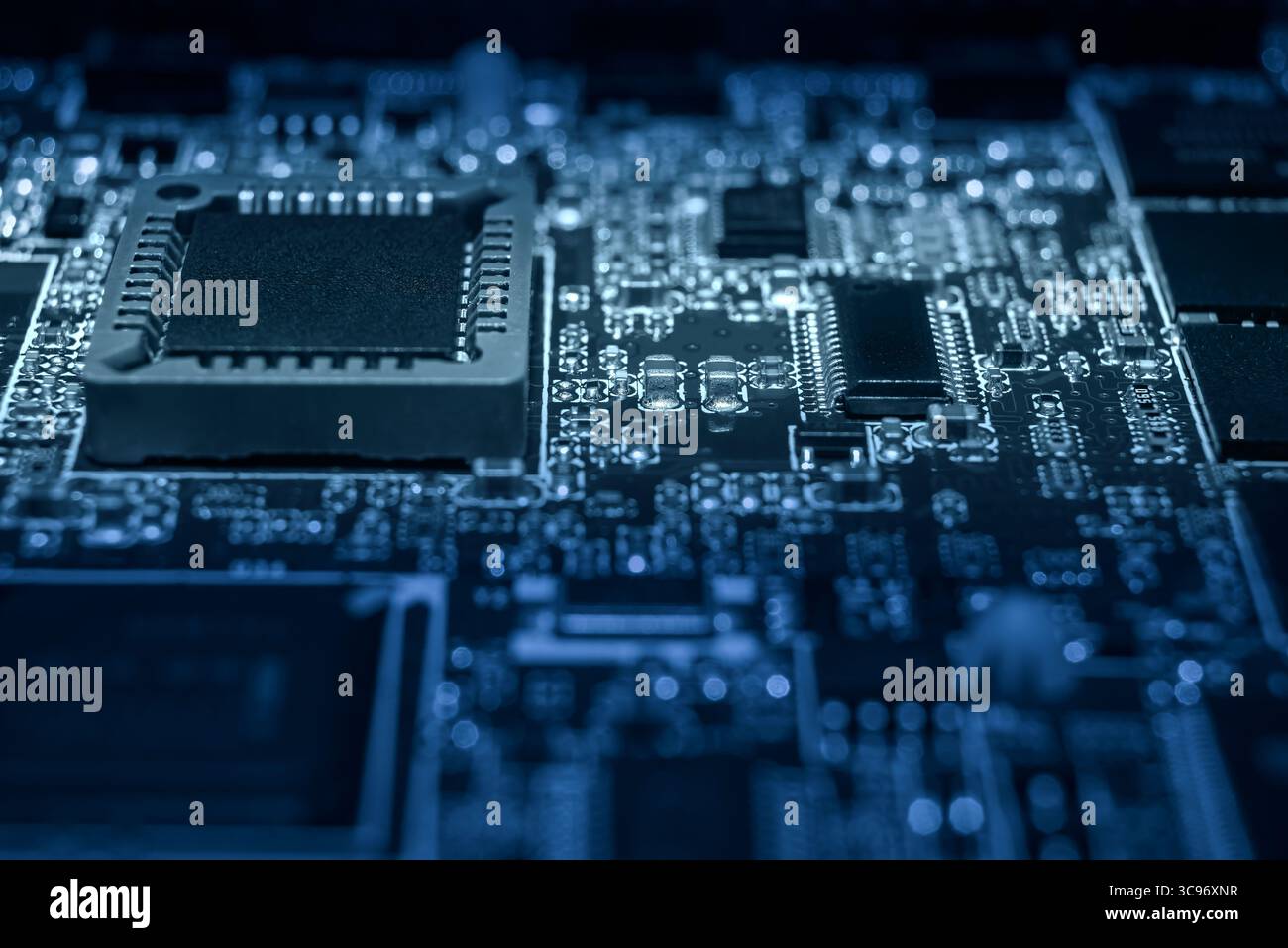 Intricate circuit board features various microchips and electronic components illuminated in blue light, showcasing advanced technology. Stock Photo