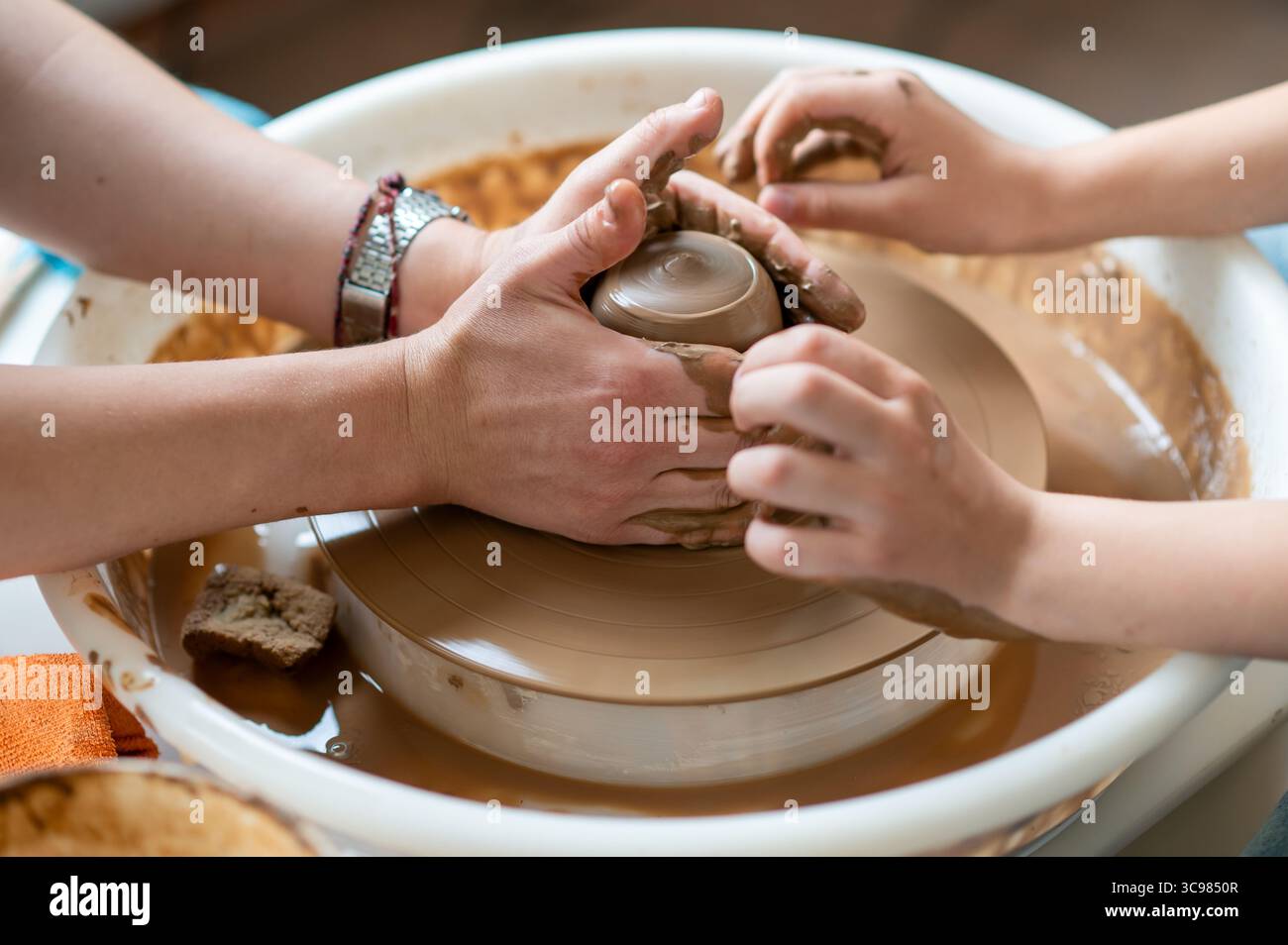 Close-up of adult and child hands together molding clay on pottery wheel, teamwork in pottery class Stock Photo