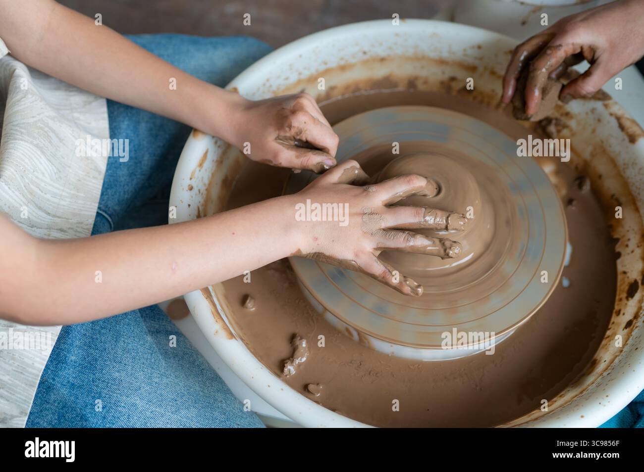 Close-up of adult and child hands together molding clay on pottery wheel, teamwork in pottery class Stock Photo