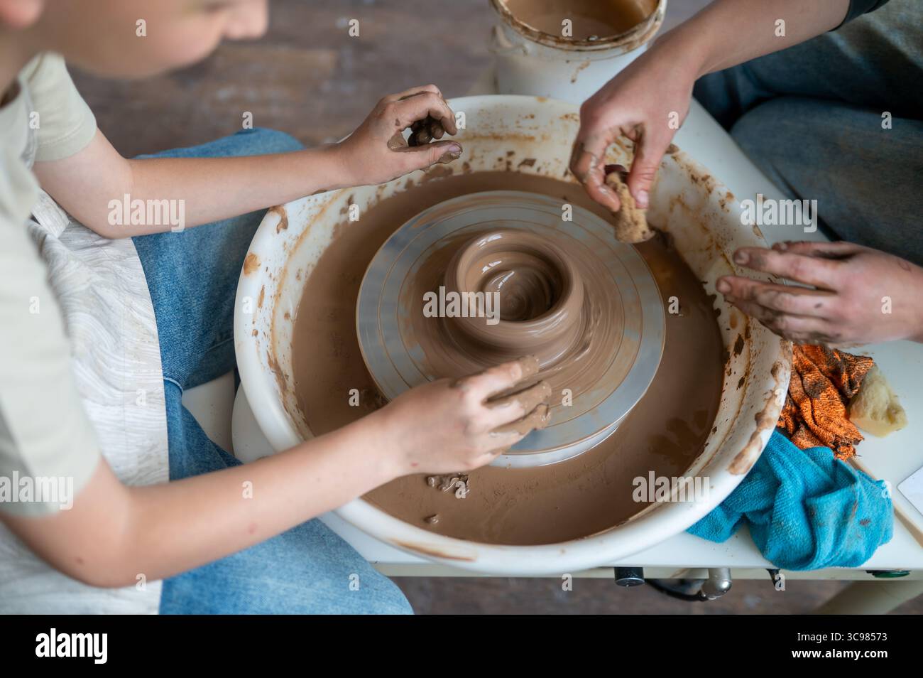Close-up of adult and child hands together molding clay on pottery wheel, teamwork in pottery class Stock Photo