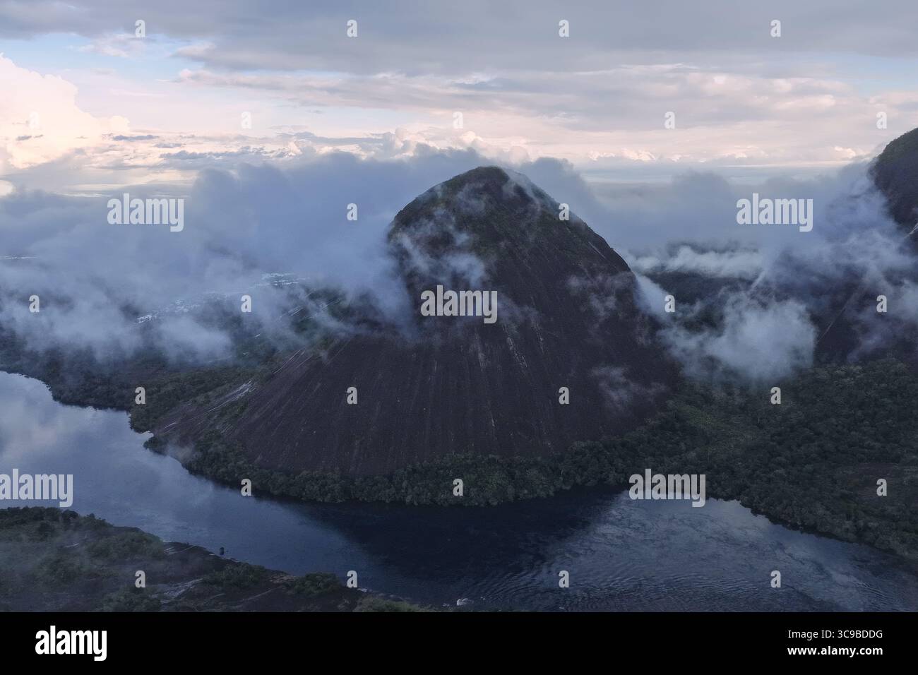Aerial view of the majestic Cerro Mono, shrouded in ethereal clouds, rises dramatically from the dark, mirror-like waters, Inirida, Guainia, Colombia. Stock Photo