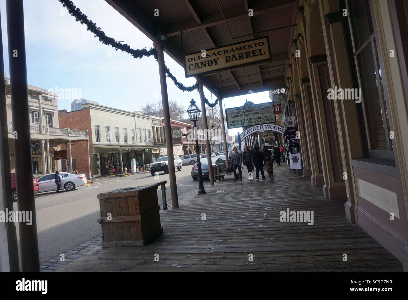 Visitors stroll along the wooden boardwalk in Old Sacramento, California, past vintage storefronts and historic buildings under clear winter skies Stock Photo