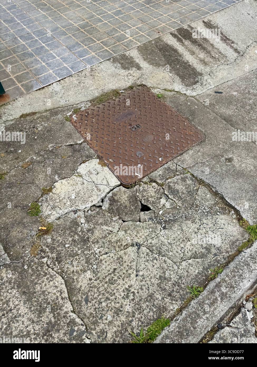 Public sanitation cover with pavement subsidence requiring urgent repair by municipal services. - Smartphone Captured Stock Image
