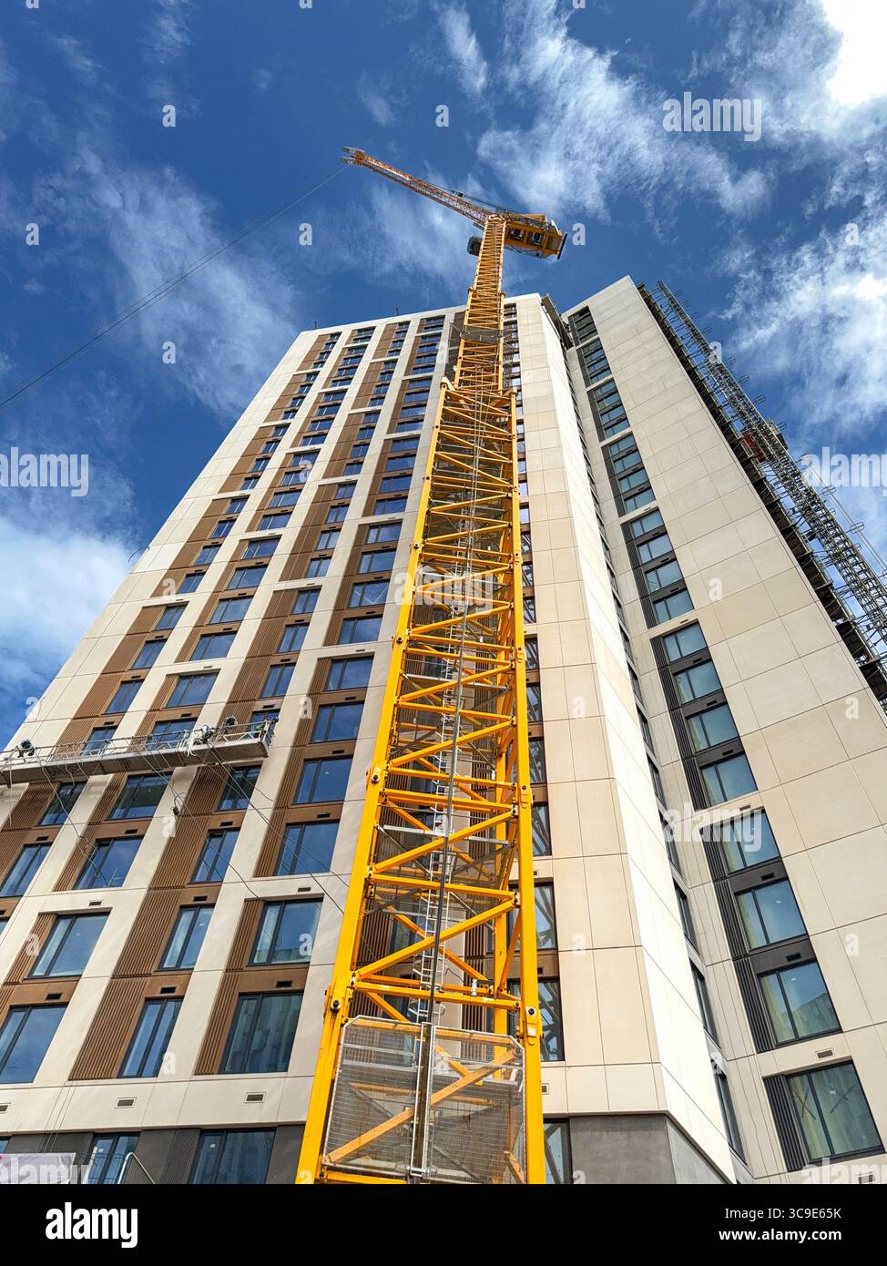 Cardiff, Wales, UK - 16 July 2025: Low angle view looking up a tall tower crane on the outside of a new block of flats in Cardiff city centre. - Smartphone Captured Stock Image