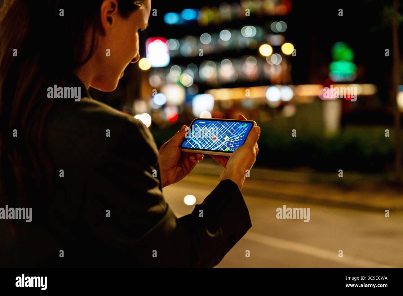 Modern urban female checking GPS map on smartphone outdoors at night Stock Photo