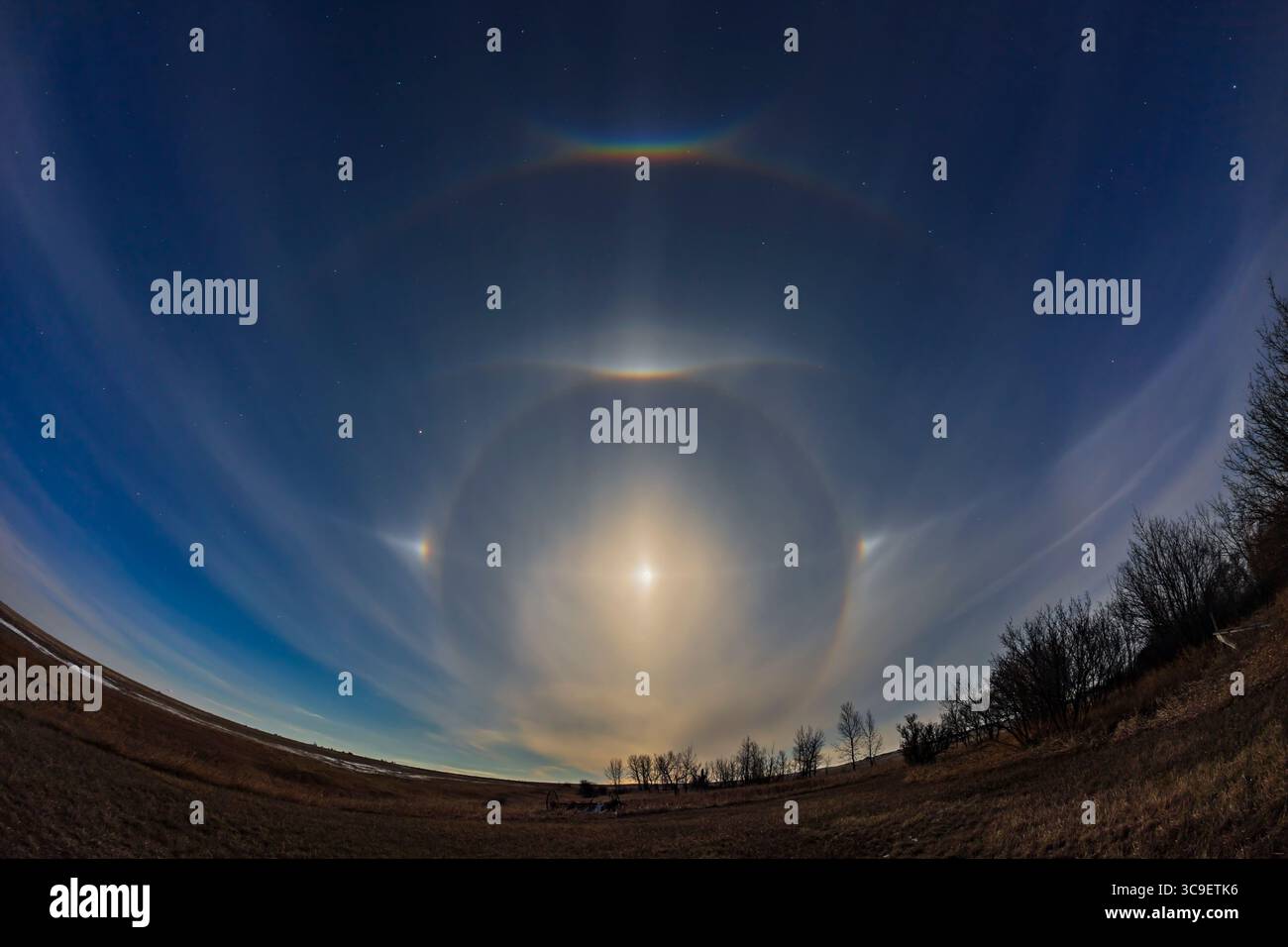 April 15, 2022, Alberta, Canada: A complex of halo phenomena on the evening of April 15, 2022, Good Friday of the 2022 Easter weekend, around the almost Full Moon. Ice crystals in the high cloud created the halos and arcs, set in the spring night sky, with the Big Dipper at top, Arcturus to the left, and Regulus and Leo at right. The colours of the arcs and sundogs were just visible to the unaided eye. ..Visible are: .â€” The 22Â° halo.â€” A large partial halo that looks like a 46Â° halo but is actually a supralateral arc. .â€” A pair of paraselene (called parhelia when they are around the Sun Stock Photo