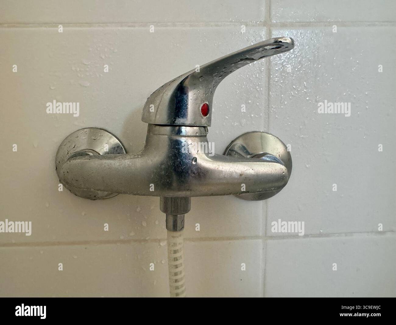 Close-up of a metal shower faucet handle mounted on a tiled bathroom wall. - Smartphone Captured Stock Image