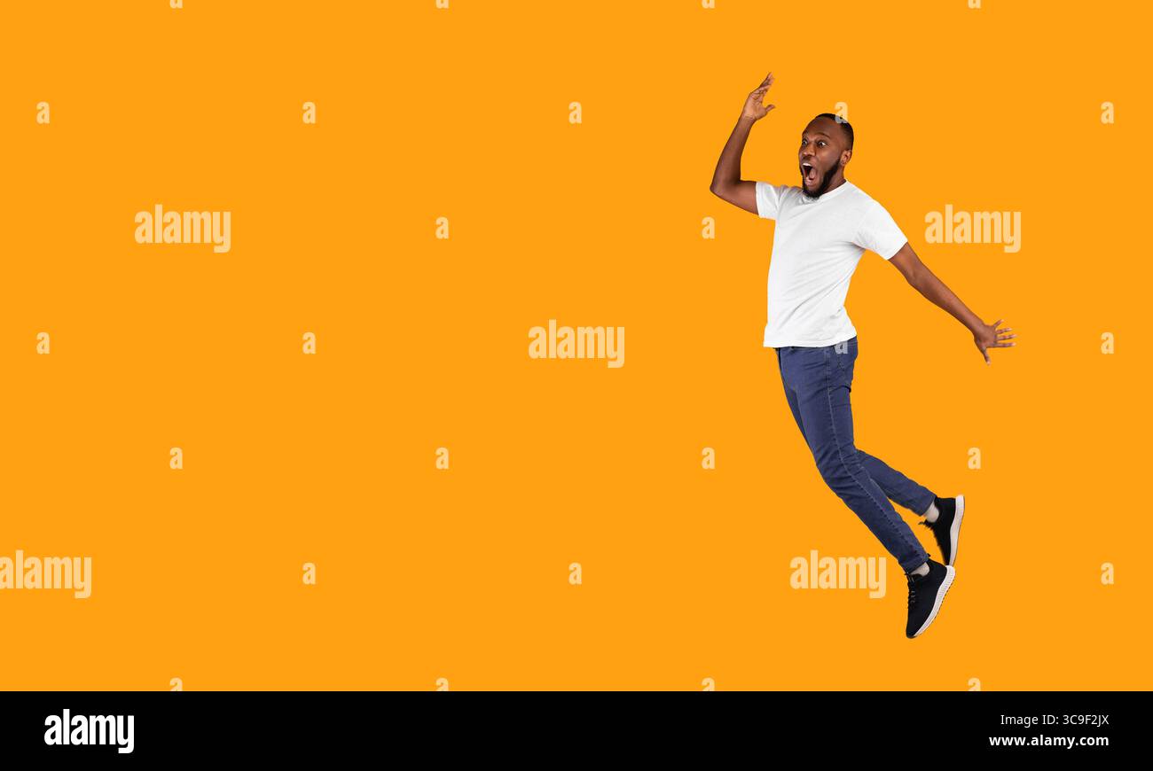 Black Guy Jumping Looking Aside In Shock On Yellow Background Stock Photo