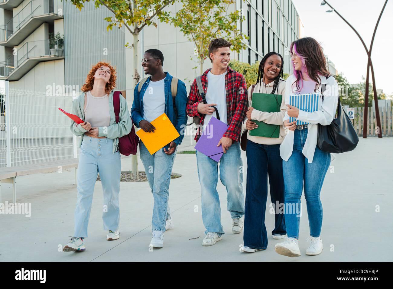 A lively group of young students enjoying their time together, smiling and sharing laughter while carrying vibrant folders and notebooks as they walk Stock Photo