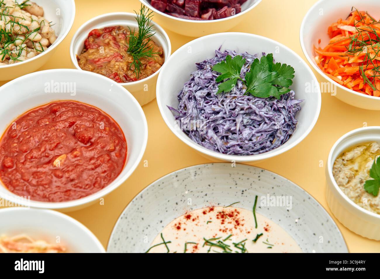 A Vibrant Array of Colorful Dishes Displayed in Bowls Featuring Fresh Vegetables, Creamy Sauces, and Savory Salsas on a Yellow Background Stock Photo