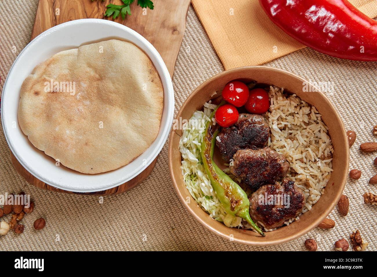 A Delicious Plate of Traditional Cuisine Featuring Grilled Meatballs, Fluffy Rice, Fresh Vegetables, and Authentic Bread Accompanied by Colorful Peppe Stock Photo