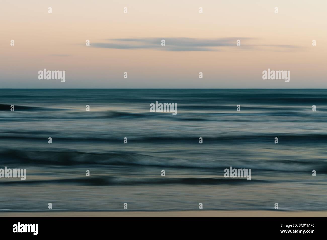 Calm ocean waves beneath a pastel-colored evening sky. Stock Photo