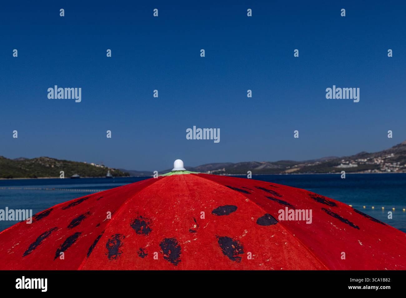 A red sun umbrella on the shore of the Adriatic Sea in Croatia on the island of Ciovo, a watermelon-shaped umbrella Stock Photo
