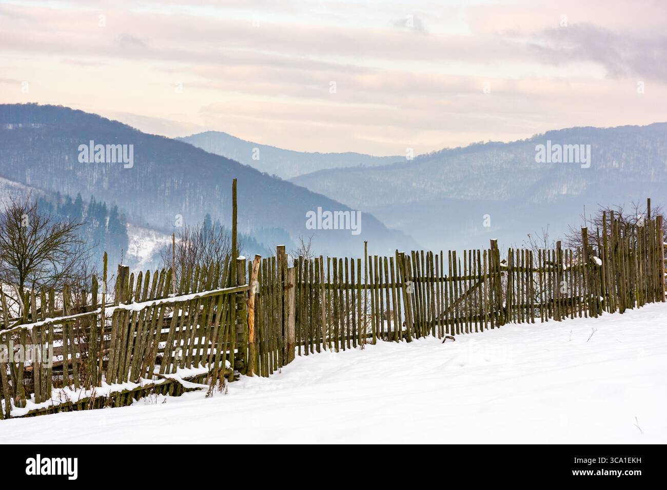 wooden fence on snow covered hill. rustic construction. mountainous carpathian countryside in winter. rural scenery Stock Photo