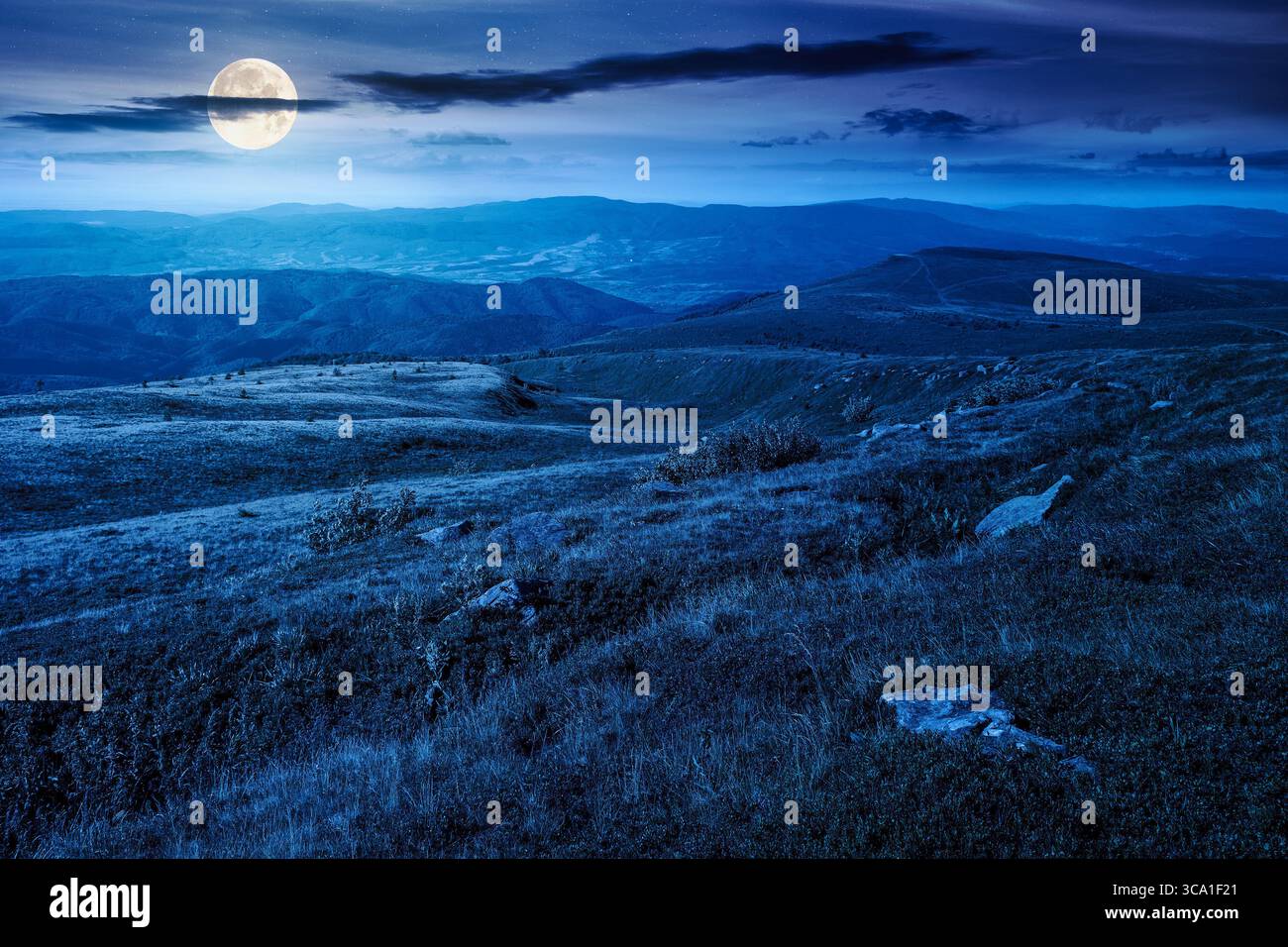 mountain landscape in summer at night. beautiful view of rolling green hills and alpine meadows in full moon light. scenery with clouds on the dark sk Stock Photo