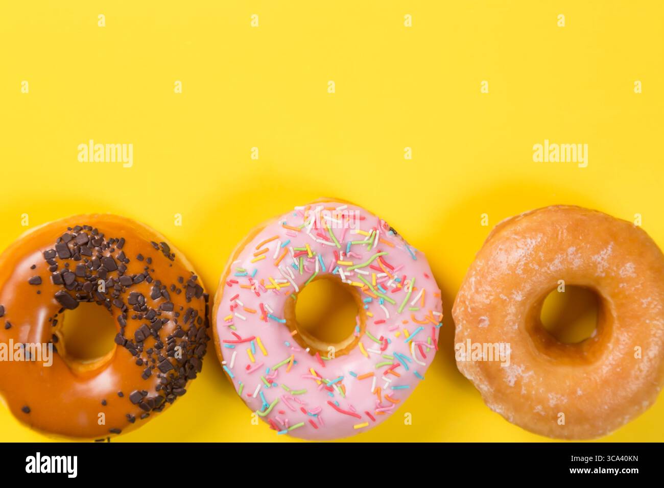 Three different donuts on yellow background. Top view and free space for text. Stock Photo