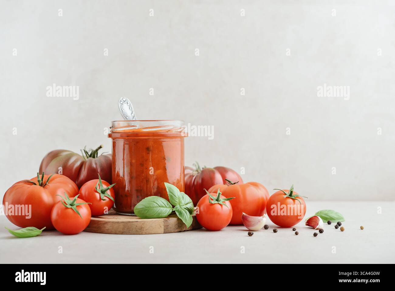 Traditional tomato sauce in a glass jar with fresh basil, ripe tomatoes, garlic and pepper on wooden cutting board, closeup Stock Photo