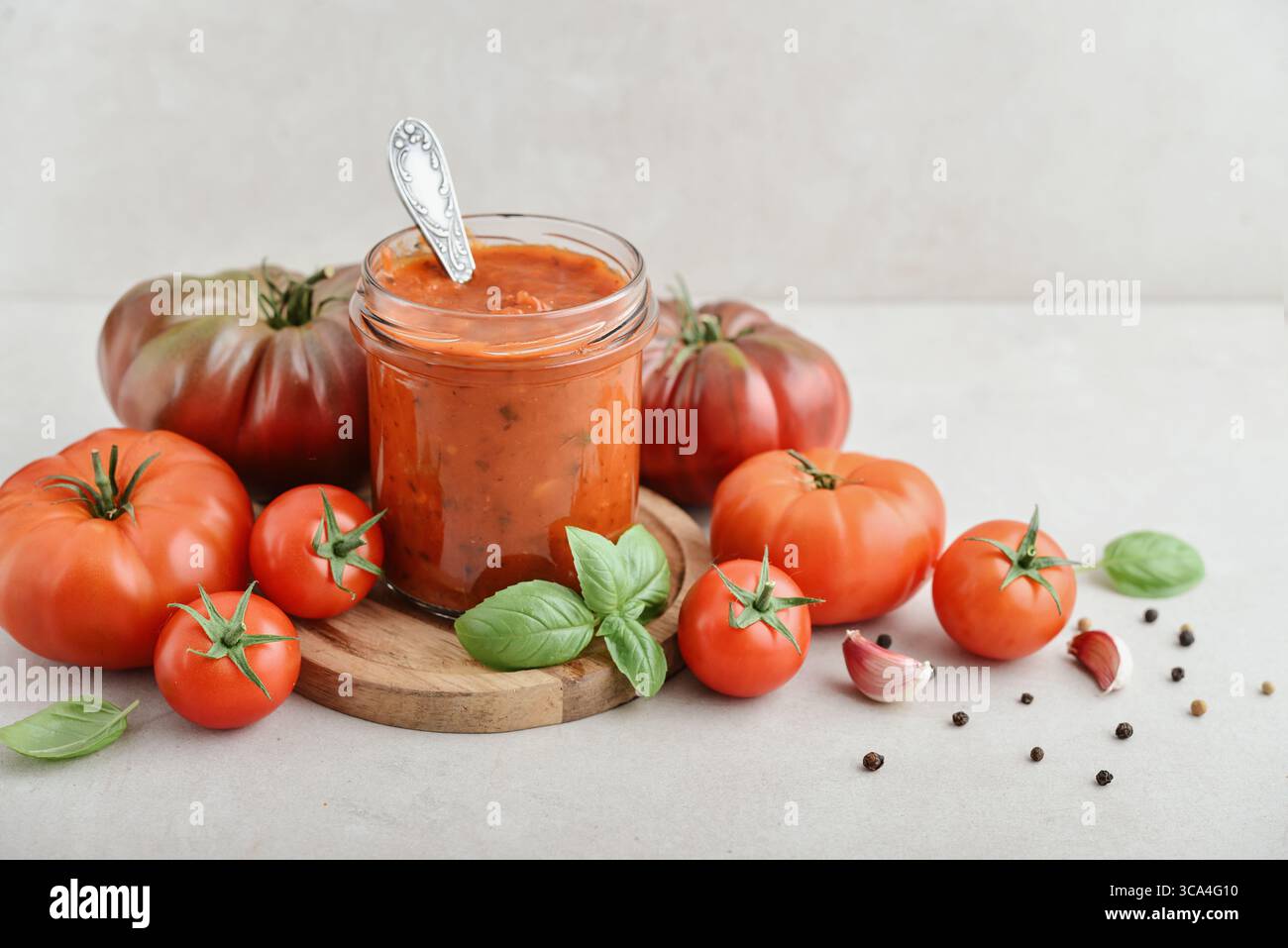 Traditional tomato sauce in a glass jar with fresh basil, ripe tomatoes, garlic and pepper on wooden cutting board, closeup Stock Photo