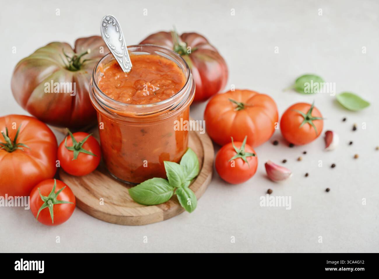 Traditional tomato sauce in a glass jar with fresh basil, ripe tomatoes, garlic and pepper on wooden cutting board, closeup Stock Photo