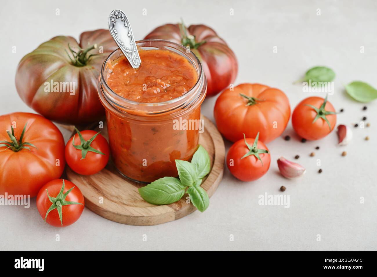 Traditional tomato sauce in a glass jar with fresh basil, ripe tomatoes, garlic and pepper on wooden cutting board, closeup Stock Photo