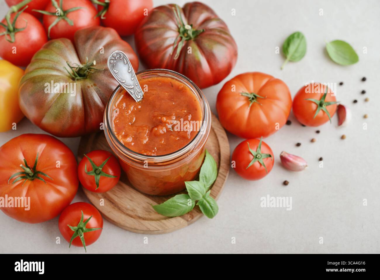 Traditional tomato sauce in a glass jar with fresh basil, ripe tomatoes, garlic and pepper on wooden cutting board, closeup Stock Photo