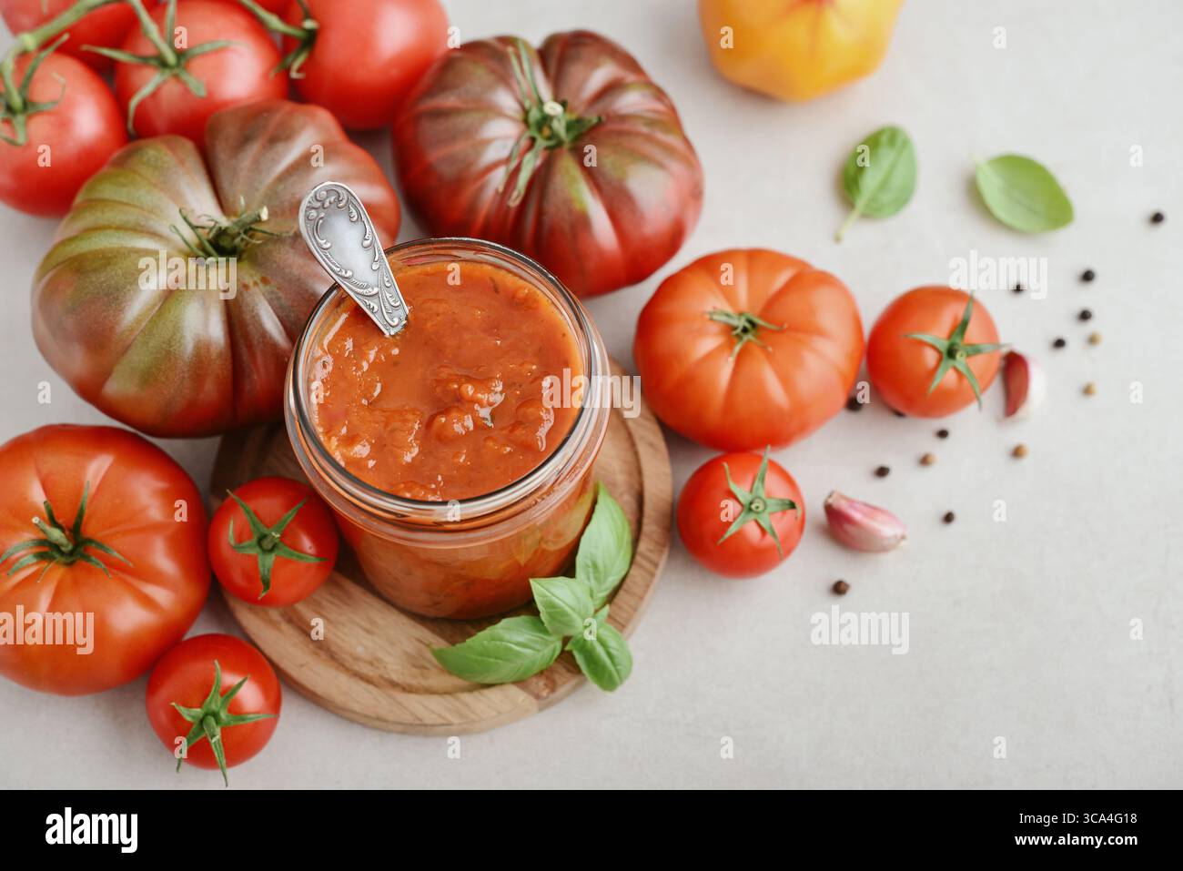 Traditional tomato sauce in a glass jar with fresh basil, ripe tomatoes, garlic and pepper on wooden cutting board, closeup Stock Photo