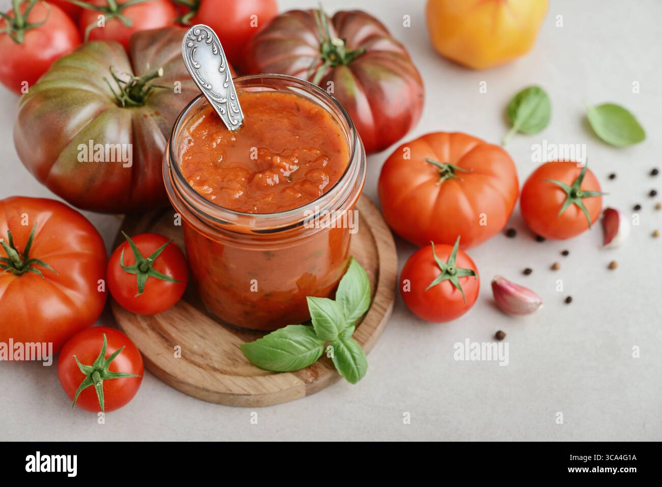Traditional tomato sauce in a glass jar with fresh basil, ripe tomatoes, garlic and pepper on wooden cutting board, closeup Stock Photo