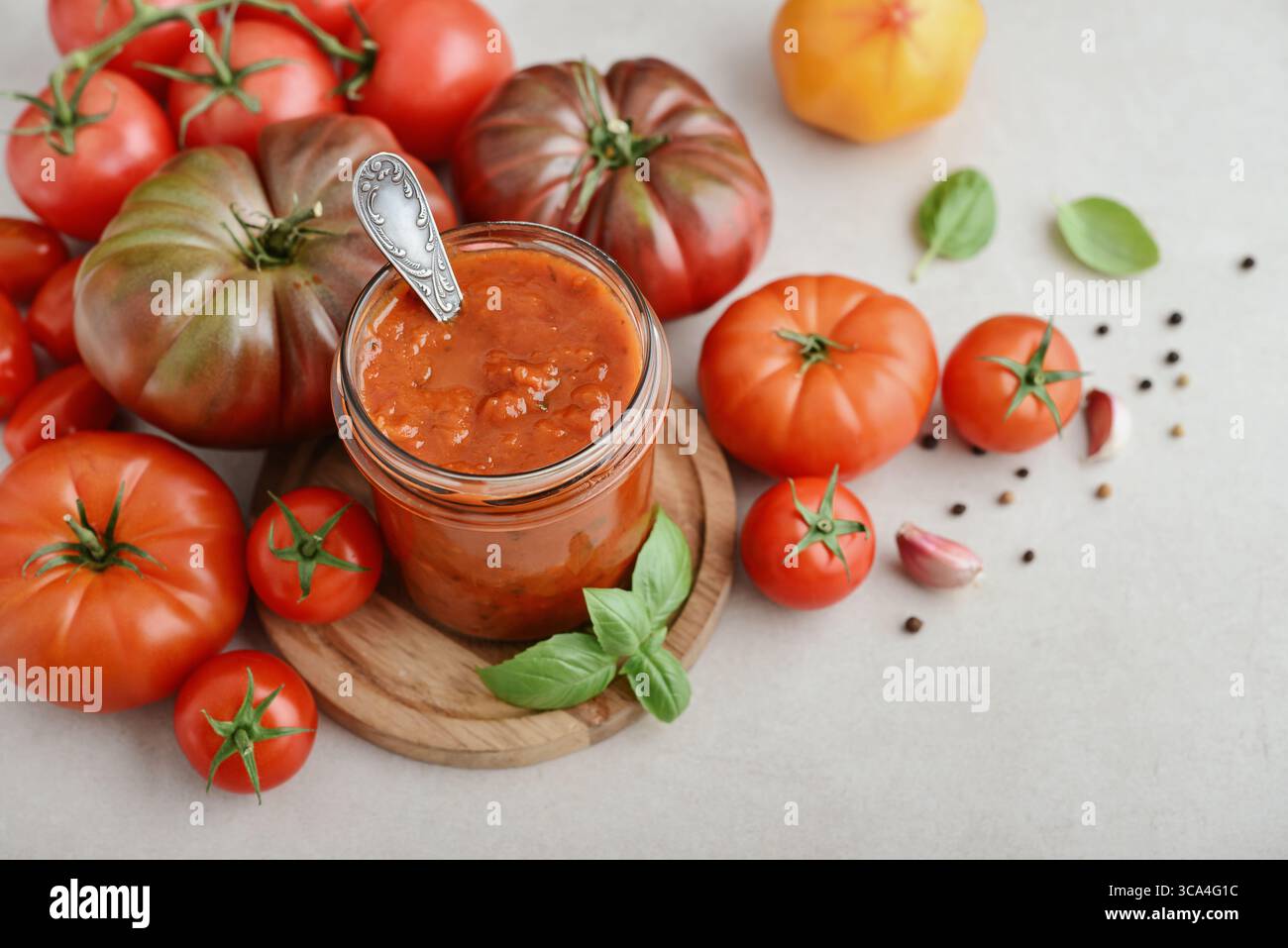 Traditional tomato sauce in a glass jar with fresh basil, ripe tomatoes, garlic and pepper on wooden cutting board, closeup Stock Photo
