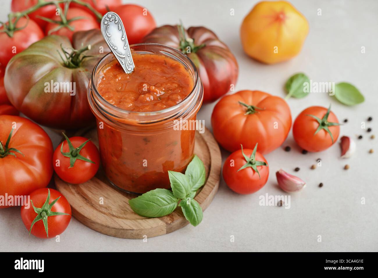 Traditional tomato sauce in a glass jar with fresh basil, ripe tomatoes, garlic and pepper on wooden cutting board, closeup Stock Photo
