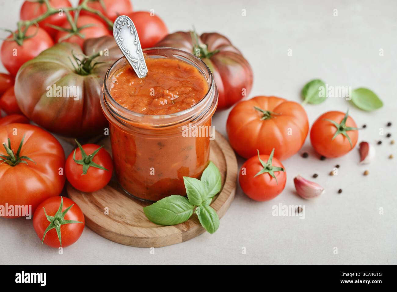 Traditional tomato sauce in a glass jar with fresh basil, ripe tomatoes, garlic and pepper on wooden cutting board, closeup Stock Photo