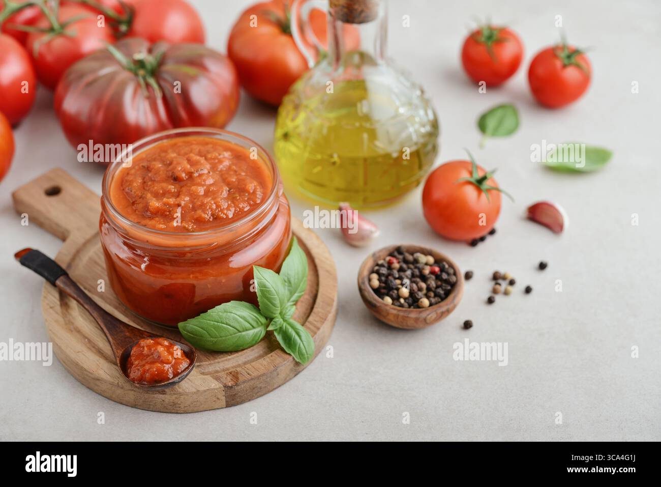 Traditional tomato sauce in a glass jar with fresh basil, ripe tomatoes, garlic and pepper on wooden cutting board, closeup Stock Photo