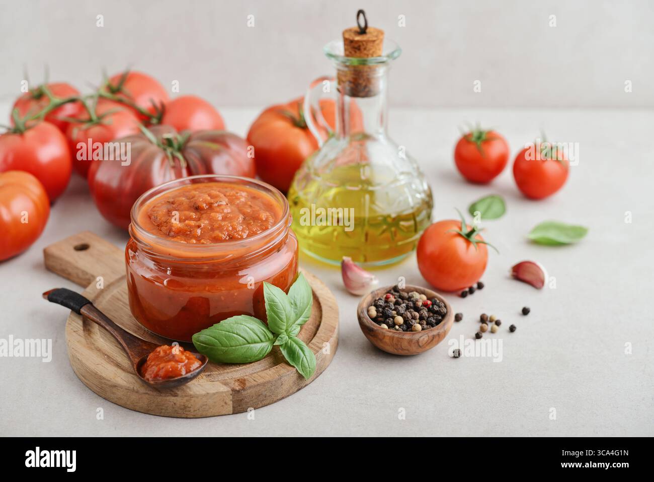Traditional tomato sauce in a glass jar with fresh basil, ripe tomatoes, garlic and pepper on wooden cutting board, closeup Stock Photo